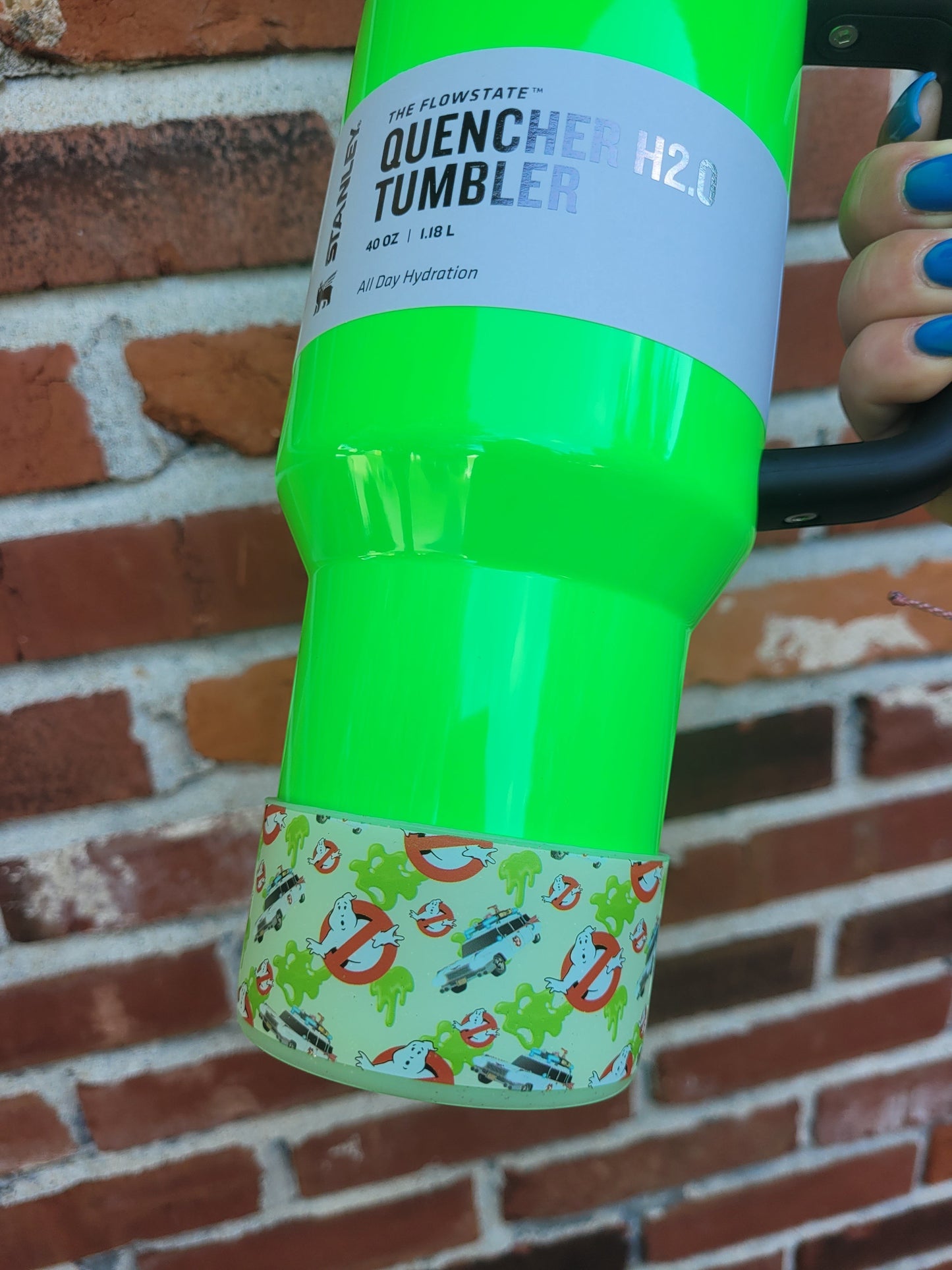 THE SALTY CHIC Ghostbusters silicone tumbler boot on a bright neon green Stanley Quencher cup against a brick wall.